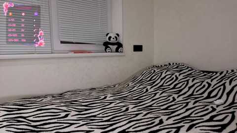 Video of a bedroom with a zebra-striped comforter, a stuffed panda on a window ledge, and a partially open venetian blind.