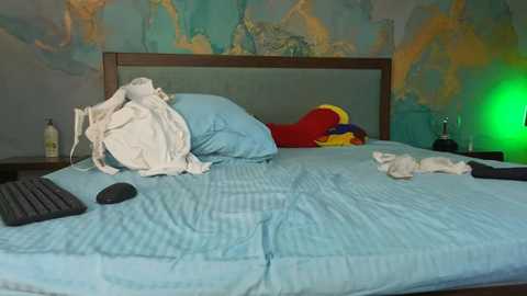 Video of a messy bedroom with a blue bedspread, a white pillow, and scattered clothes, including a red shirt, against a colorful, world map-themed wall.