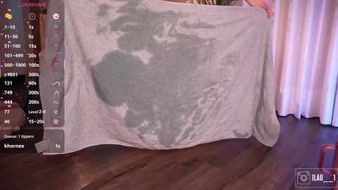A video shows a person holding a light gray towel with a faint map of Australia printed on it, standing in a room with wooden floors and white curtains.