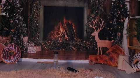Video of a cozy, festive living room with a lit fireplace, Christmas tree, deer statue, and wrapped presents; a glass candleholder and a pair of black shoes are scattered on the beige rug.