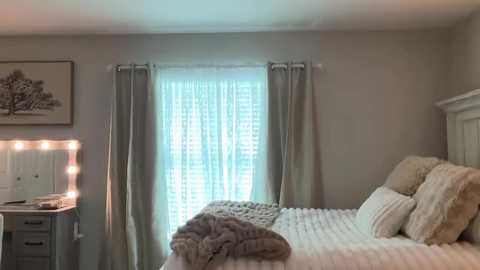 Video of a cozy bedroom with a white bed, beige curtains, a wall-mounted mirror, and a wooden nightstand.