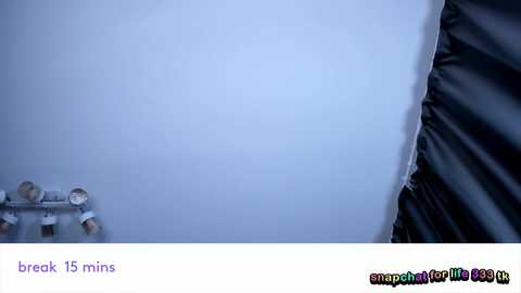 A video showing a white wall with a small, black, rectangular object on the left, likely a camera, and a partially visible, dark, textured surface on the right. The bottom text reads \"break 15 mins.\