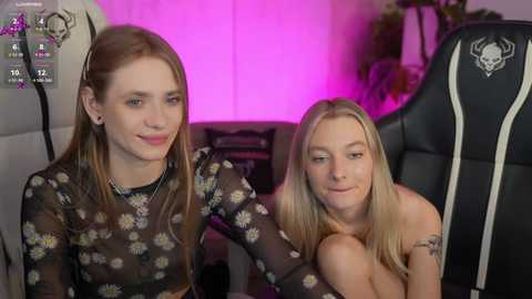 Media: Video of two young women with long, straight hair, one wearing a floral top and the other topless, sitting in gaming chairs under purple lighting in a dimly lit room.