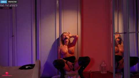 A topless, fair-skinned woman with blonde hair, wearing only black stockings and high heels, sits on a stool in front of a mirror, casting a shadow. The room has dim lighting with purple and red hues.