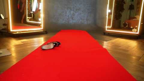 Video of a bright red carpet stretching towards a mirror, reflecting two people in a dimly lit room with wooden floors and warm lighting.