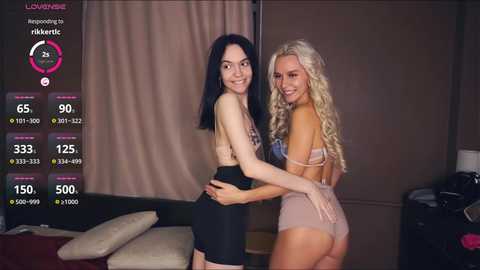 Video of two women in lingerie, one with black hair, the other with blonde curls, in a modern bedroom setting.