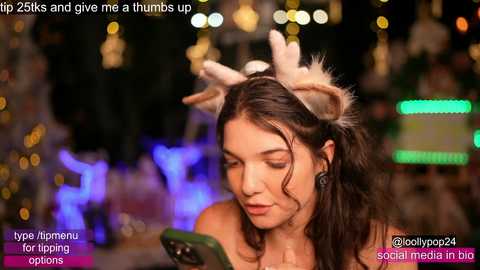 A video shows a young woman with wavy brown hair, wearing a reindeer headband and earphones, looking at a smartphone. The background is blurred with festive lights and text overlays promoting a YouTube channel.