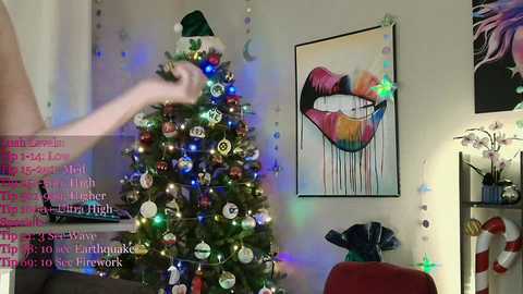 Video of a festive, decorated Christmas tree with colorful lights and ornaments in a living room, featuring a large, colorful abstract painting of lips and a green hat.