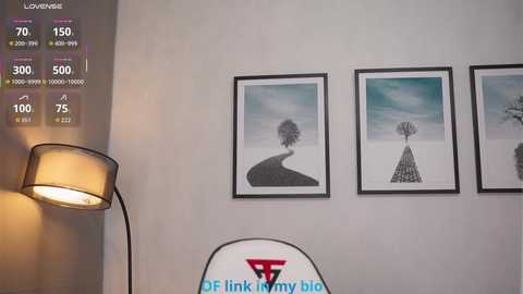 A video of a minimalist room with a white wall displaying three minimalist tree art prints and a modern lamp, set against a backdrop of weather app data.