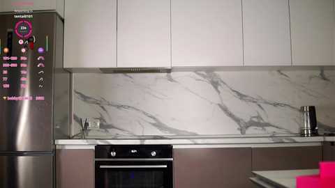 Video of a modern kitchen with white cabinets, marble backsplash, stainless steel appliances, and a pink countertop.