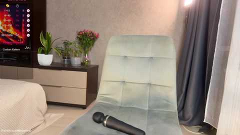 Video of a modern bedroom with a light blue chaise lounge, a TV showing a colorful screen, a potted plant, and a black vibrator on the floor.