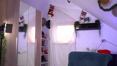 Video of a cozy attic bedroom with white walls, wooden wardrobe, mirrored ceiling, and hanging plants; soft purple lighting.