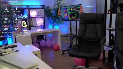 Video of a vibrant, modern gaming room with a black ergonomic chair, colorful monitors, neon heart lights, and pink balloons on the floor.