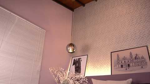Media: A video of a modern bedroom corner featuring a textured silver wallpaper, a pendant light, a framed black-and-white photo, and blinds.