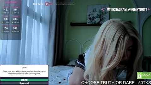 A video depicts a blonde woman with long hair lying on a bed, wearing a black and white striped shirt, in a dimly lit bedroom. Text overlays read \"Choose Truth or Dare-50KTK.\