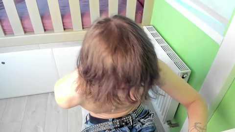 Video of a young woman with shoulder-length brown hair, wearing a sleeveless top and jeans, standing in a room with light-colored walls and a white radiator.