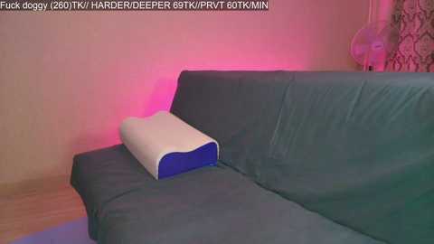 A video showing a teal sofa with a white lumbar pillow emitting a pink glow against a beige wall, with text in the top left corner.
