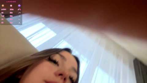 A close-up video of a woman with light skin, long blonde hair, and prominent eyelashes, taken from a low angle, showing a blurred background. The image is slightly out of focus, with a digital interface overlay in the top left corner.