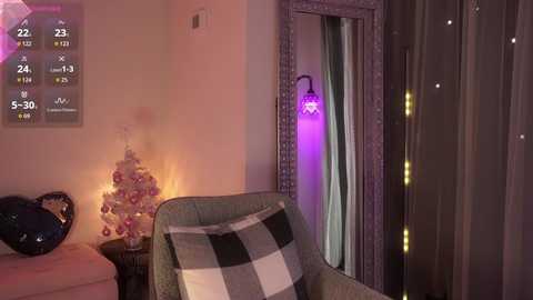 A video of a cozy living room with a white Christmas tree, a plaid throw, a lit candle, a mirror, and a glowing purple lamp.