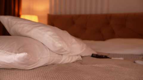 Video of a plush, beige, tufted headboard bed with white pillows and a beige blanket, featuring a warm, ambient light from a lamp in the background.