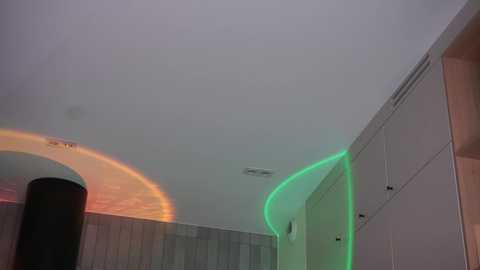 Video of a modern room with white walls, a tall cylindrical black lamp, and glowing green and orange light circles on the ceiling, creating a dynamic, ethereal ambiance.