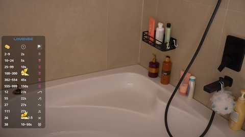 Video of a beige-tiled bathroom with a white bathtub, showerhead, and shelf holding bottles of shampoo, conditioner, and body wash. A digital overlay shows a game screen with a yellow bird.