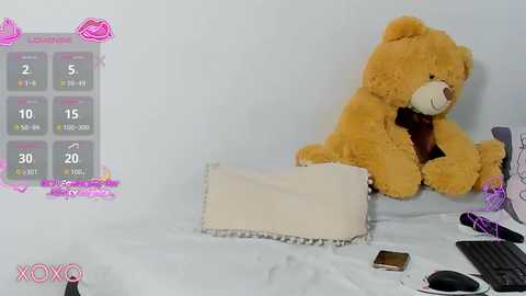 A video of a plush teddy bear and a white pillow on a white bed, with a pink \"XOXO\" graphic and a game interface in the corner.