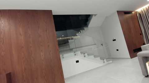 Video of a modern, minimalist living room with white walls, wooden paneling on one wall, and a spiral staircase leading upstairs. The space is clean and sleek, with a neutral color palette and a hint of natural light.