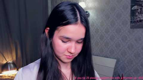 Video of a young Asian woman with long black hair, wearing a white top, in a dimly lit bedroom with a patterned wallpaper, a lit candle, and text overlay.