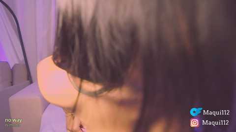 Video of a woman with long black hair and a petite physique, wearing glasses, seen from a low angle, with a soft, purple-toned background.