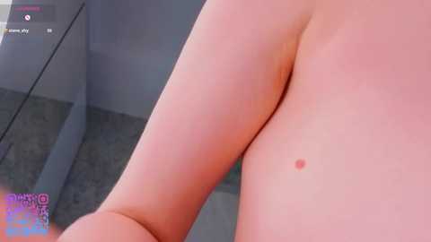 A video of a light-skinned person's back with a small, red mole, taken indoors with a gray carpet and glass table visible in the background.