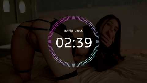 Media: Video of a woman in black lingerie, bent over on a bed, with a \"02:39\" digital clock overlay. Dimly lit room with blurred background.