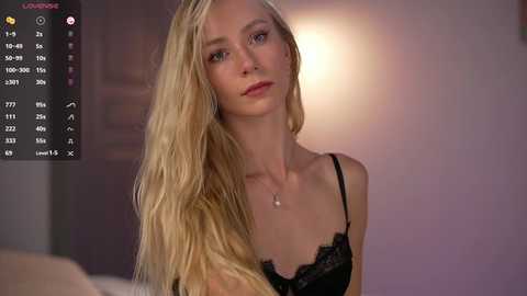 Video of a blonde, fair-skinned woman with long hair, wearing a black lace bra, indoors, soft lighting.