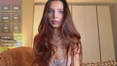 Video of a young woman with long brown hair, wearing a white lace bra, standing in a bedroom with a beige wardrobe and a brown bear toy.