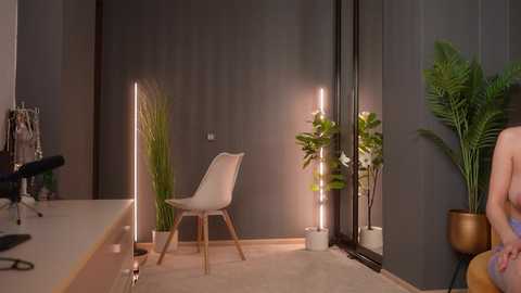 Video of a modern, minimalist office with a gray wall, a white chair, and a tall floor lamp. A potted plant sits near a large mirror.