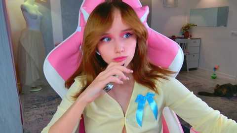 Video of a young girl with long brown hair, wearing a pink gaming chair, pink shirt, and blue earrings, sitting in a cozy, well-lit room with a mirror and colorful toys.