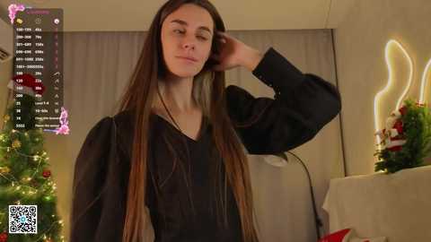 Video of a slender, long-haired woman with pale skin and a relaxed expression, wearing a black dress. Background includes a festive Christmas tree, glowing candles, and a QR code in the lower left corner.