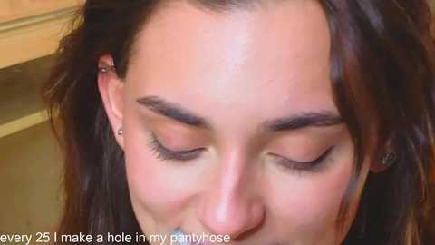 Video of a close-up of a young woman with fair skin, closed eyes, and straight brown hair, wearing small hoop earrings. Text reads: \"every 28, make a hole in my navlebone.\