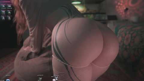 Video of a woman in a suggestive pose, leaning forward with her backside prominently displayed in tight, revealing underwear, in a dimly lit, cozy bedroom setting.