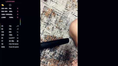 A video showing a close-up of a person's right forearm and hand holding a black object, on a textured, multi-colored carpet.