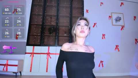 A video of a light-skinned woman with short blonde hair in a black off-the-shoulder top, standing in a festive room with red bows and gift boxes, temperature display visible.