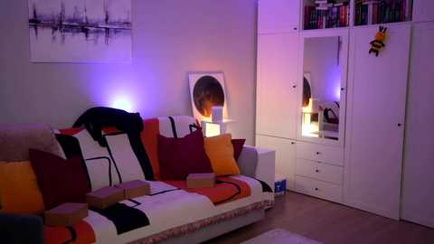 Video of a modern, cozy living room with a white sofa, red and orange pillows, a large mirror, and a colorful abstract painting on the wall.