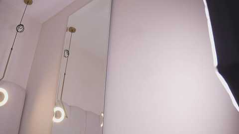 Video of a modern bathroom with a large, rectangular mirror on the right wall, two circular pendant lights with white bulbs hanging from the ceiling, and soft, diffused lighting.