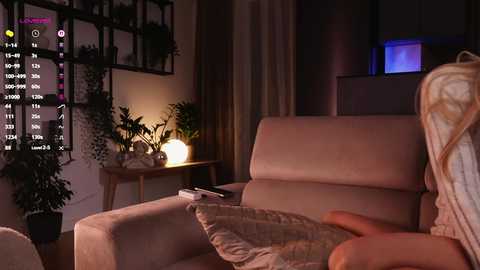 Video of a dimly lit living room with a beige couch, potted plants, a wooden side table, and a glowing lamp, showcasing a cozy ambiance.