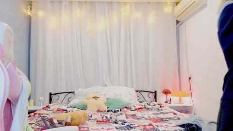 Video of a cozy, child-friendly bedroom with a white canopy bed, teddy bear, colorful quilt, and string lights; a person in a pink shirt stands in the foreground.