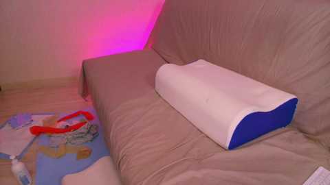 Video of a beige couch with a white and blue foam wedge pillow. A colorful children's rug with world map design is on the floor. Pink ambient lighting.