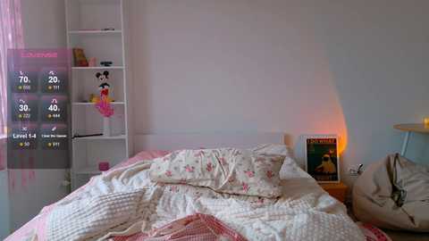 Video of a cozy, white-walled bedroom with a plush bed, pink floral bedding, and a digital clock showing 10:30. Adjacent shelves hold toys and a panda plushie, with a warm lamp casting a soft glow.