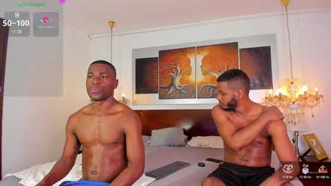 Video of two shirtless Black men on a bed in a dimly-lit room; one is resting, the other hugging him.