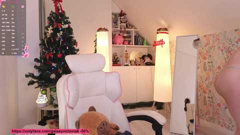 Video of a cozy, Christmas-themed bedroom with a white recliner, a lit candle, a festive tree, and a warm, white-lit room.