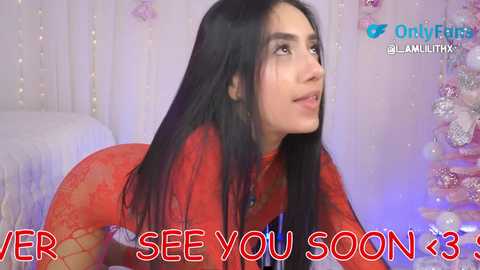 Video of a young woman with long black hair, wearing a red lace dress, kneeling on a bed in a room with pastel decor and fairy lights. Text overlays read \"VER SEE YOU SOON <3\".